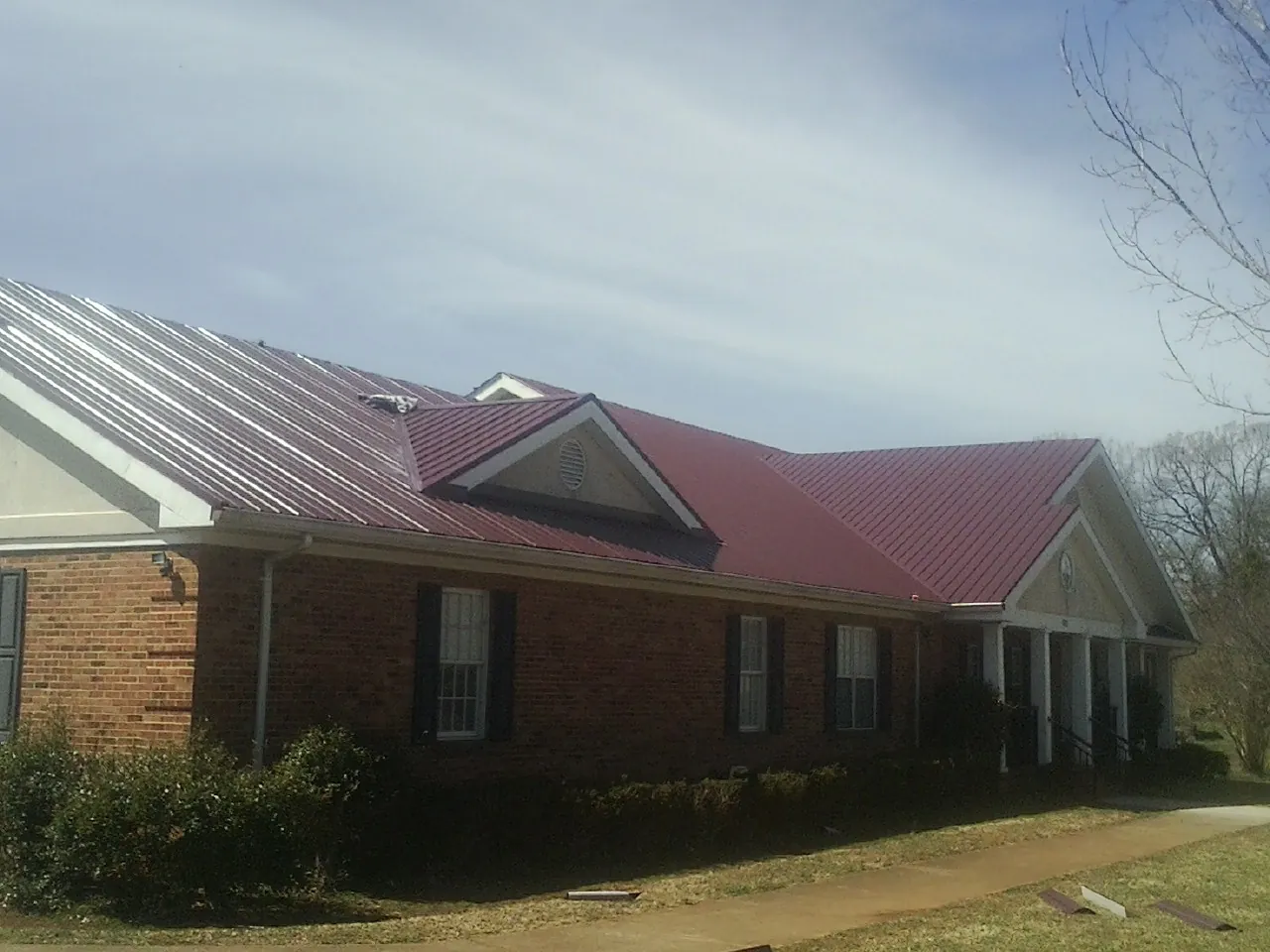 Red metal roof with gabled entries on a long brick building, from a Hail Damage Roof Repair job in Honolulu
